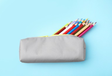 Many colorful pencils in pencil case on light blue background, top view