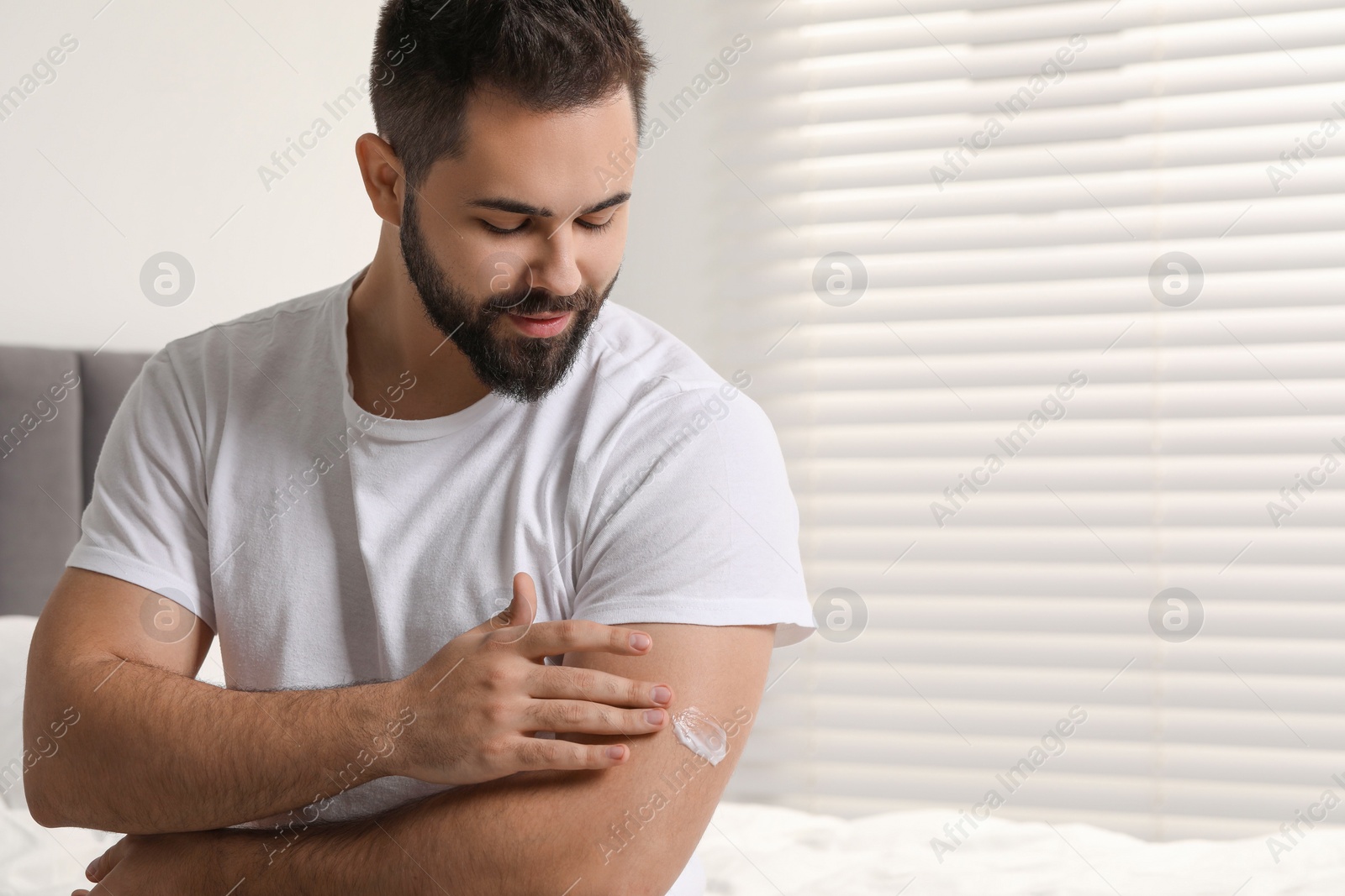 Photo of Man with dry skin applying cream onto his arm indoors, space for text