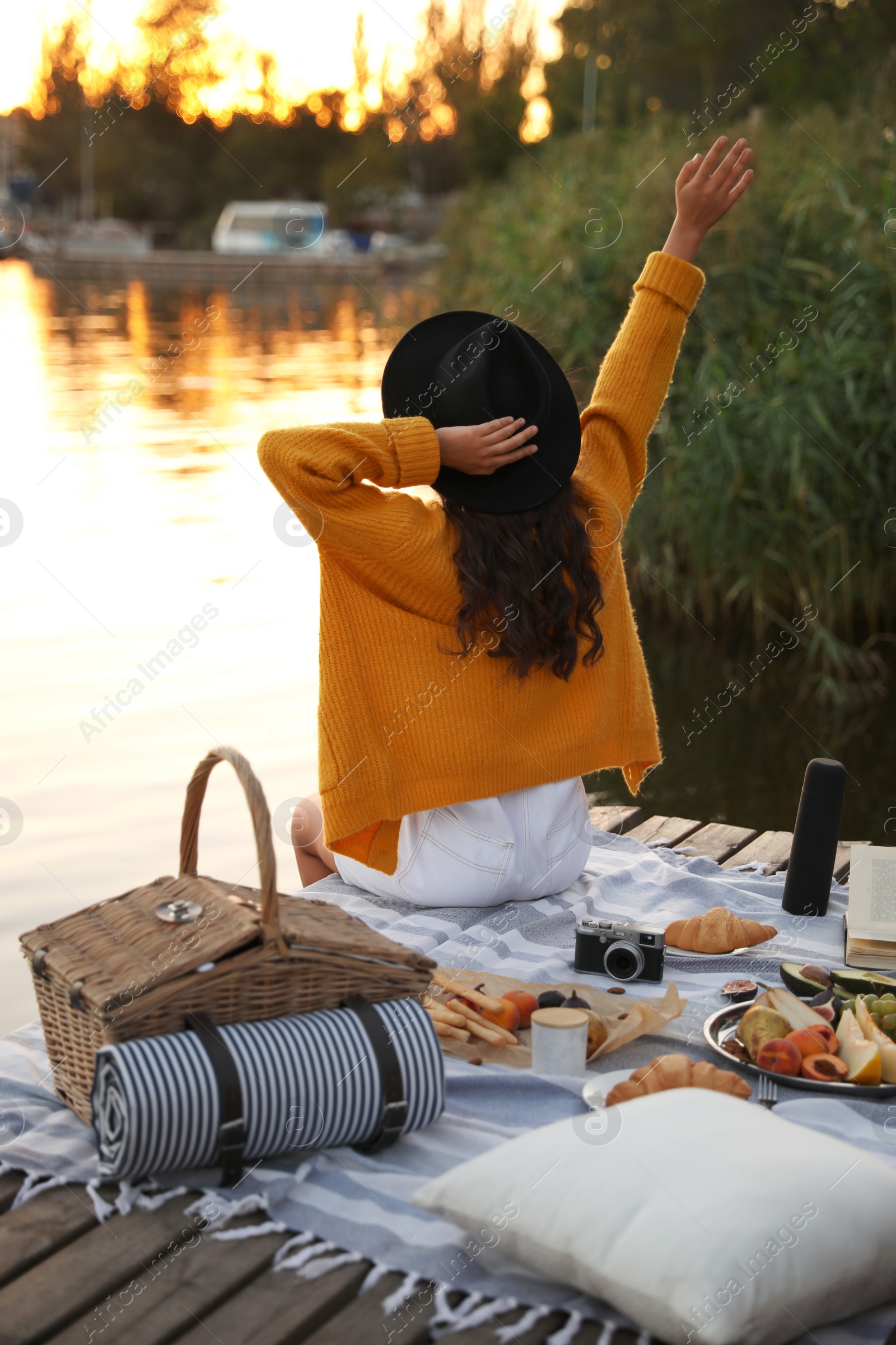 Photo of Young woman spending time on pier at picnic, back view