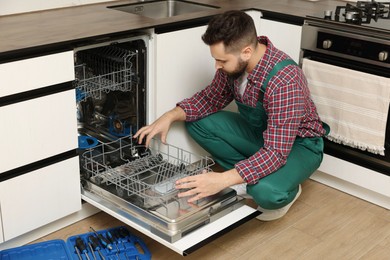 Serviceman examining dishwasher lower rack in kitchen