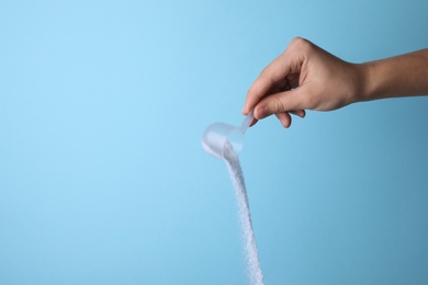 Photo of Woman pouring laundry detergent from measuring container against blue background, closeup. Space for text