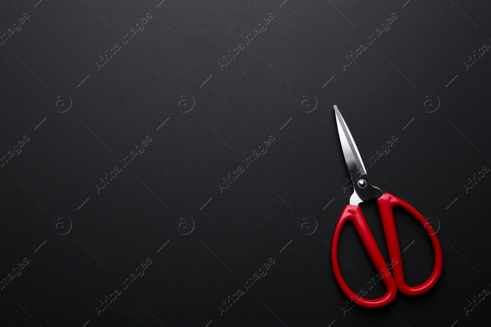 Photo of Pair of sharp scissors on dark background, top view. Space for text