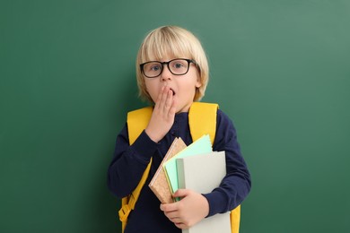Photo of Emotional little school child with notebooks near chalkboard