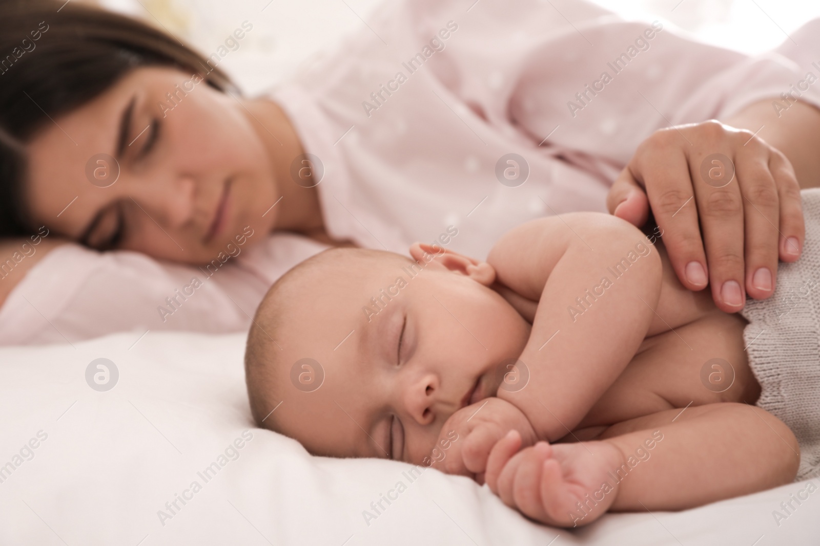 Photo of Young mother resting near her sleeping baby on bed at home