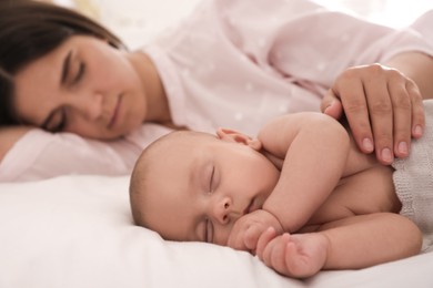 Young mother resting near her sleeping baby on bed at home