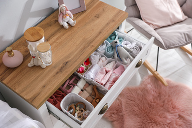 Photo of Modern open chest of drawers with baby clothes and accessories in room, above view