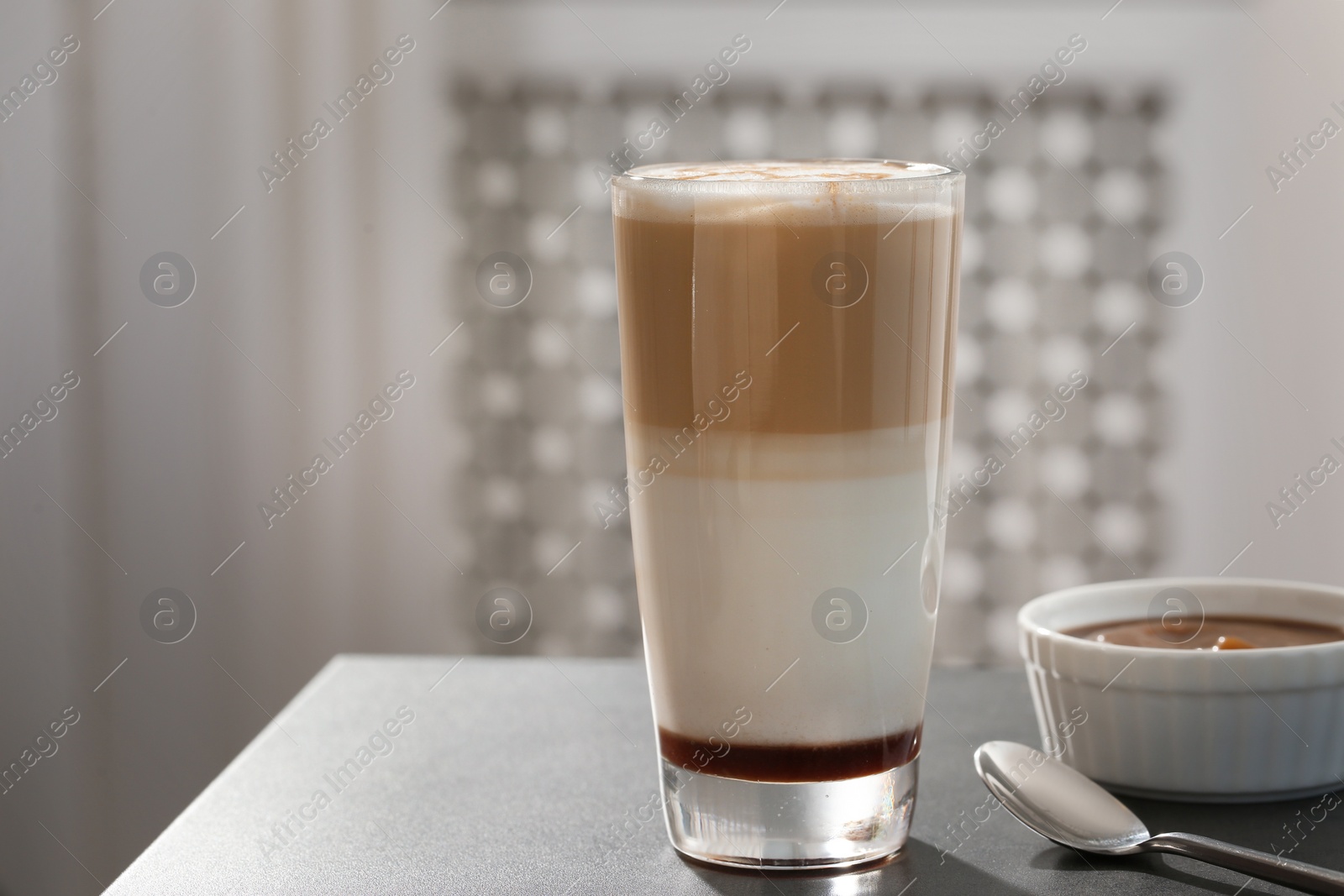 Photo of Glass of tasty caramel macchiato and syrup on table. Space for text