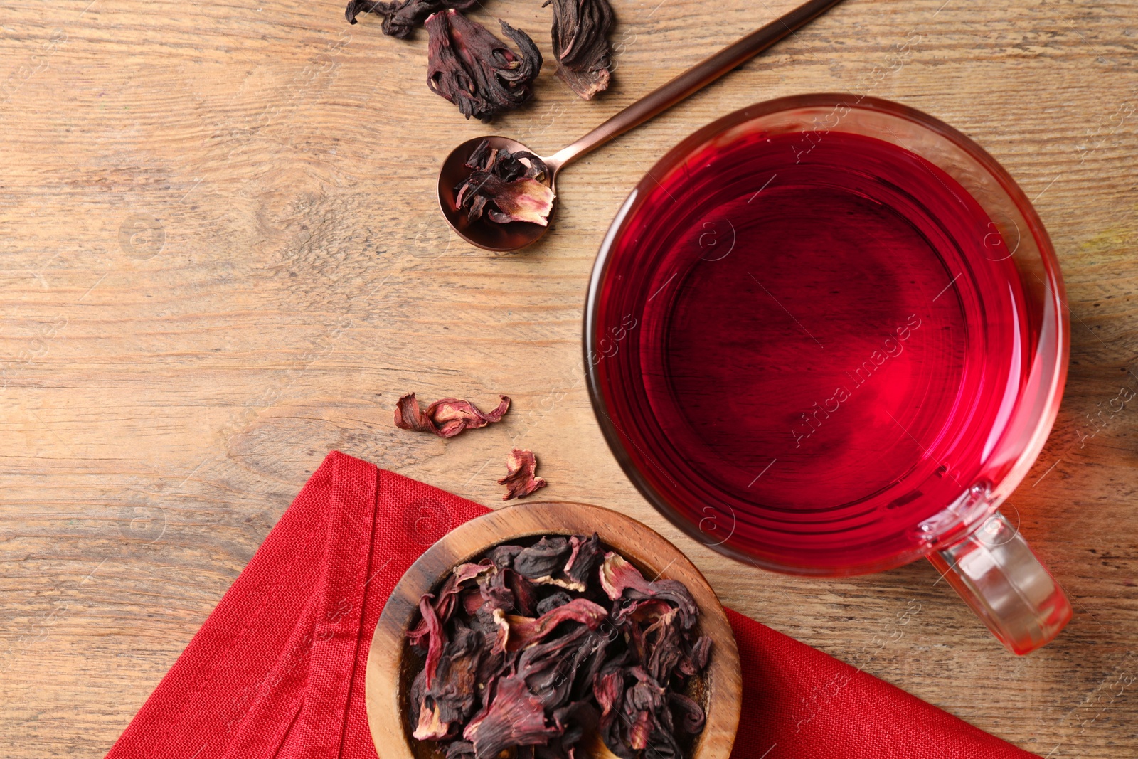 Photo of Cup of fresh hibiscus tea and dry flower leaves on wooden table, flat lay. Space for text