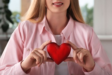 Young woman holding red heart indoors, closeup. Volunteer concept