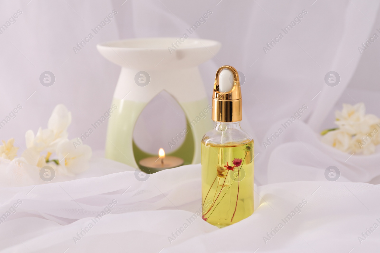 Photo of Aroma lamp and freesia essential oil on white cloth, space for text