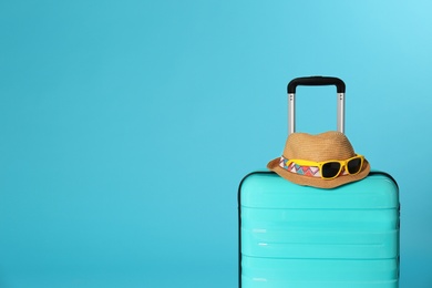 Stylish suitcase with hat and sunglasses on color background. Space for text