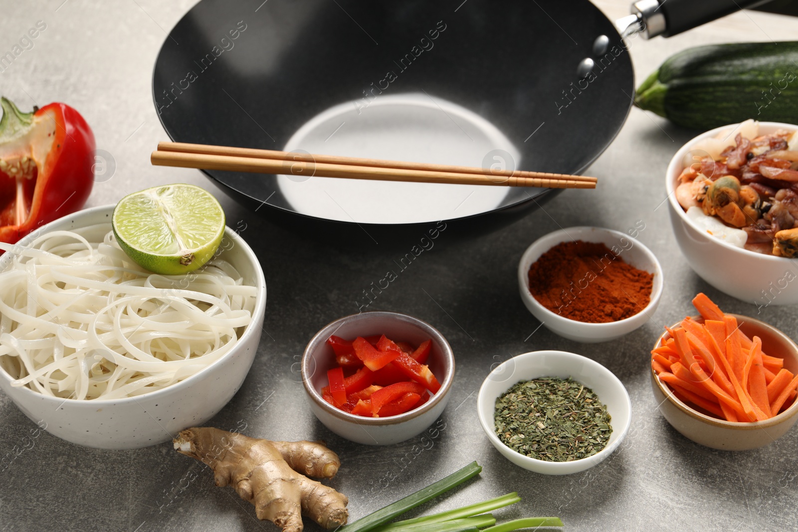 Photo of Black wok, spices and products on grey textured table, closeup