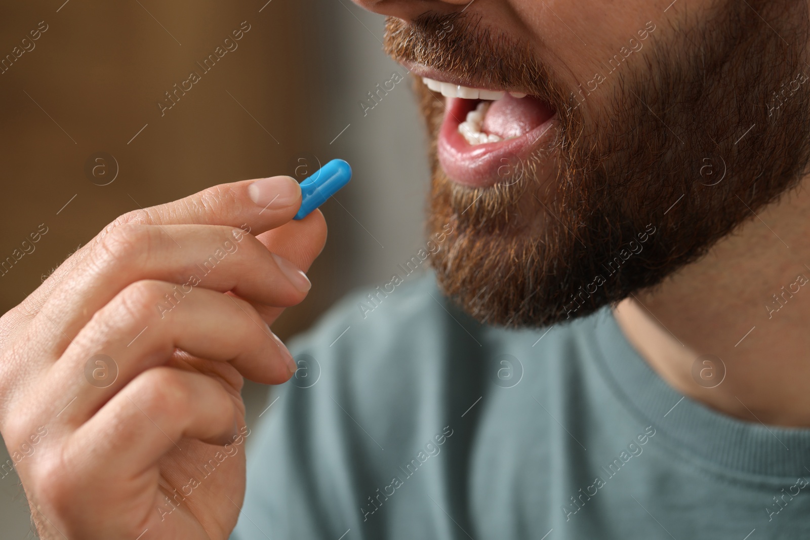 Photo of Closeup view of bearded man taking pill on blurred background