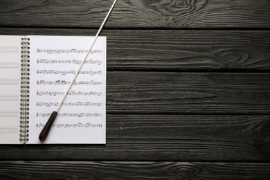 Photo of Conductor's baton and sheet music book on black wooden table, top view. Space for text