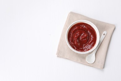 Photo of Organic ketchup in bowl and spoon on white table, top view with space for text. Tomato sauce