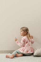 Photo of Little girl drawing on beige wall indoors. Child`s art