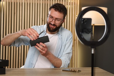 Photo of Smiling technology blogger recording video review about smartphones at home