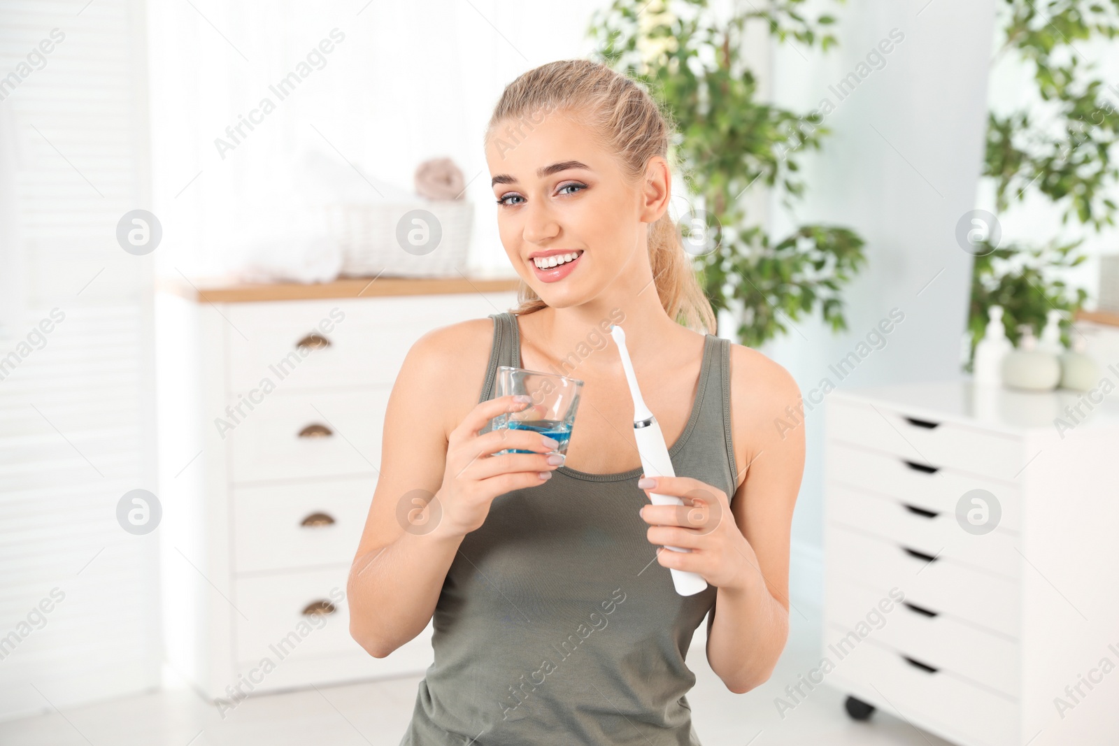 Photo of Woman holding glass with mouthwash and toothbrush in bathroom. Teeth care