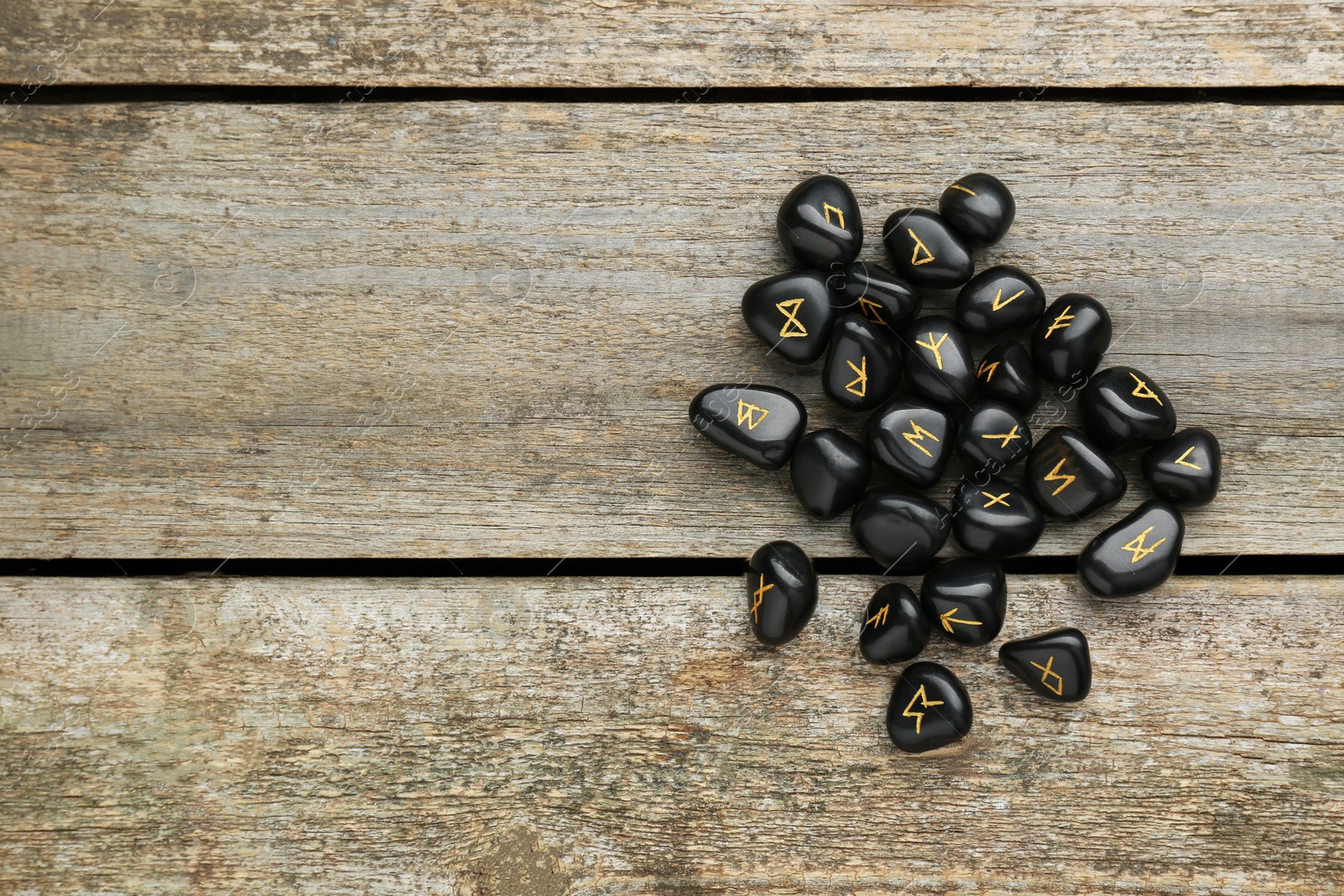 Photo of Pile of black rune stones on wooden table, flat lay. Space for text