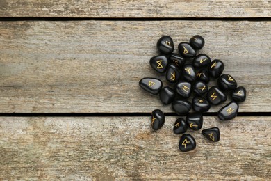 Photo of Pile of black rune stones on wooden table, flat lay. Space for text