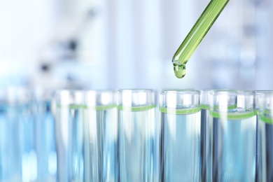 Photo of Dripping liquid into test tube on blurred background, closeup. Laboratory analysis