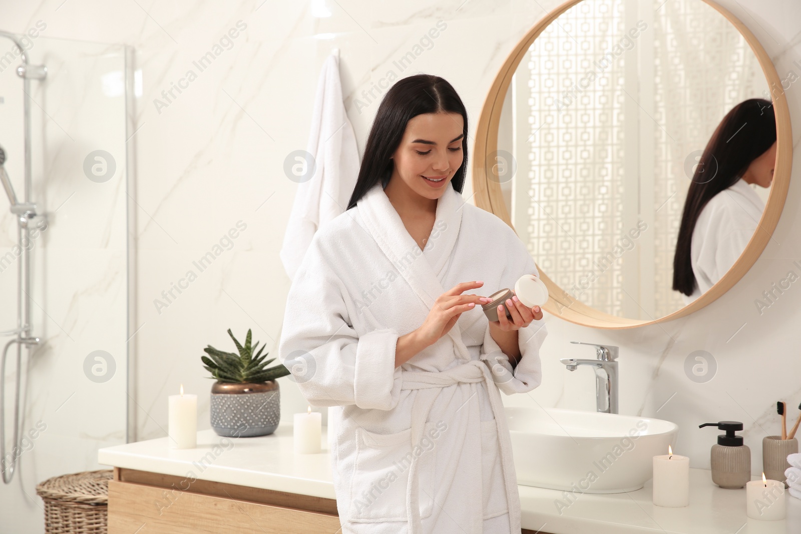 Photo of Beautiful young woman with jar of cream near mirror in bathroom