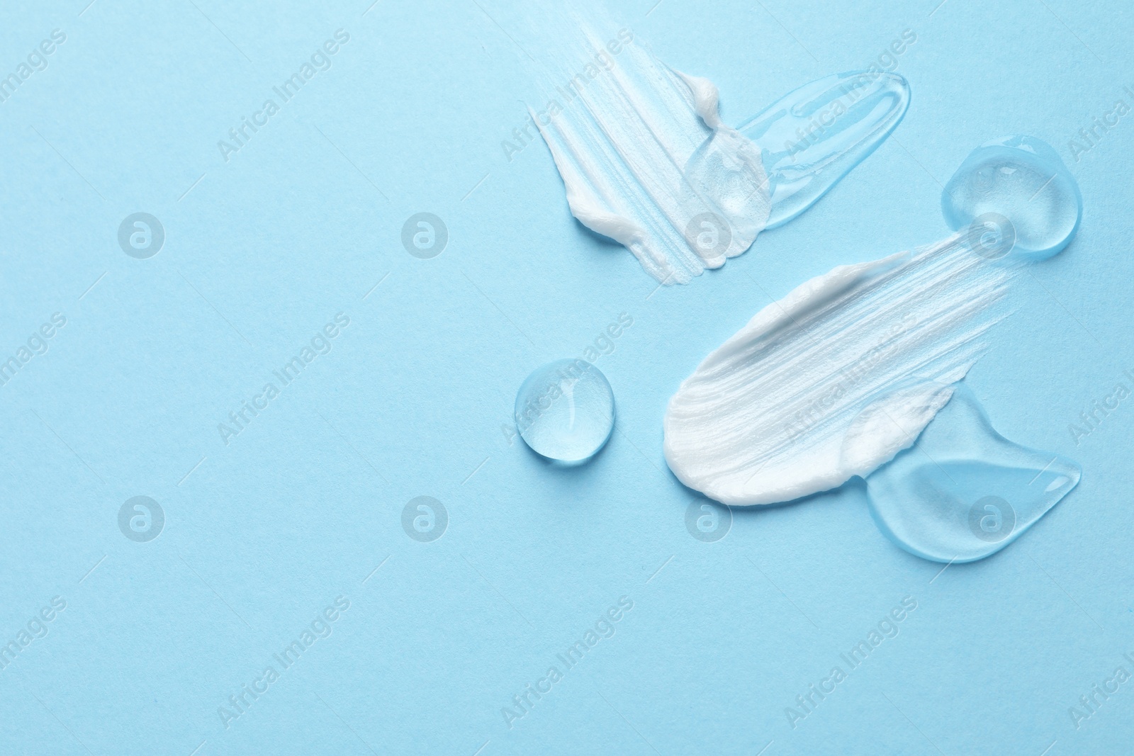 Photo of Samples of cosmetic gel and cream on light blue background, top view. Space for text