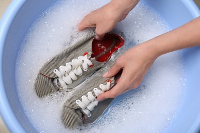 Photo of Woman washing sport shoes in plastic basin, top view