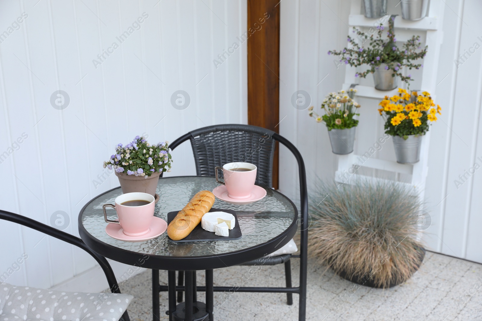 Photo of Cups of coffee, potted plant, bread and cheese on glass table. Relaxing place at outdoor terrace