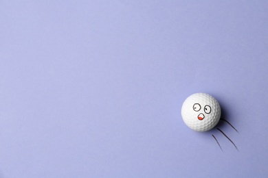 Photo of Golf ball with funny face flying on lilac background - creative image. Top view