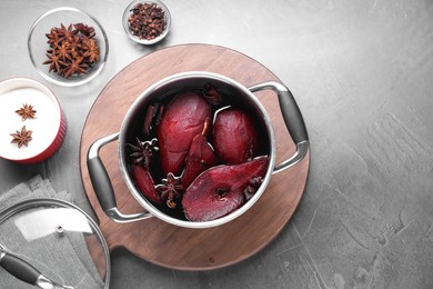 Photo of Tasty red wine poached pears and spices in pot on grey table, flat lay. Space for text