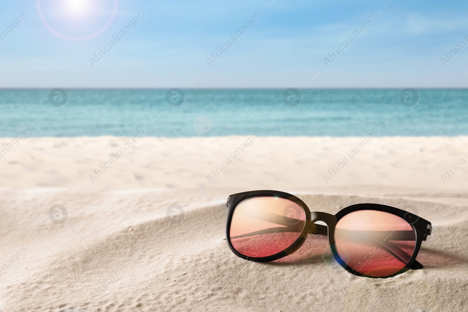 Image of Stylish sunglasses on sandy beach near sea, space for text