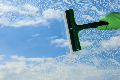 Woman cleaning glass with squeegee indoors, closeup