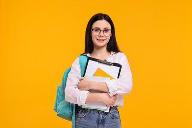 Smiling student with notebooks and clipboard on yellow background