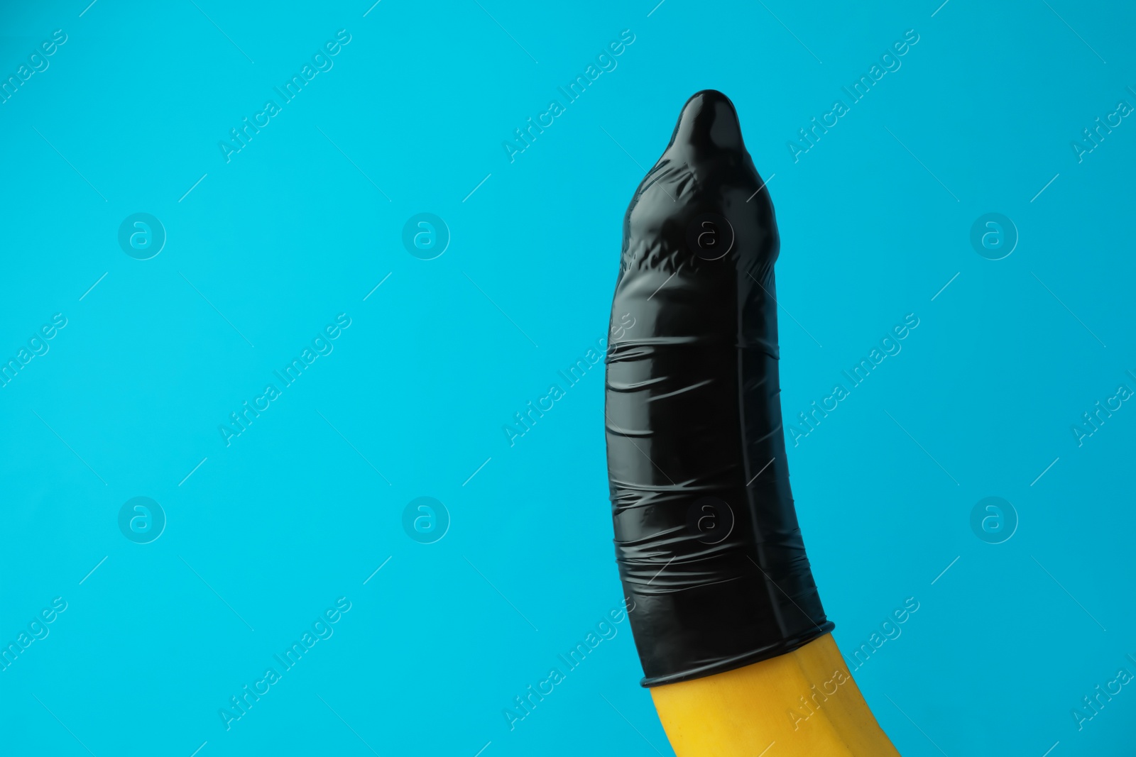 Photo of Banana with condom on light blue background, space for text. Safe sex concept