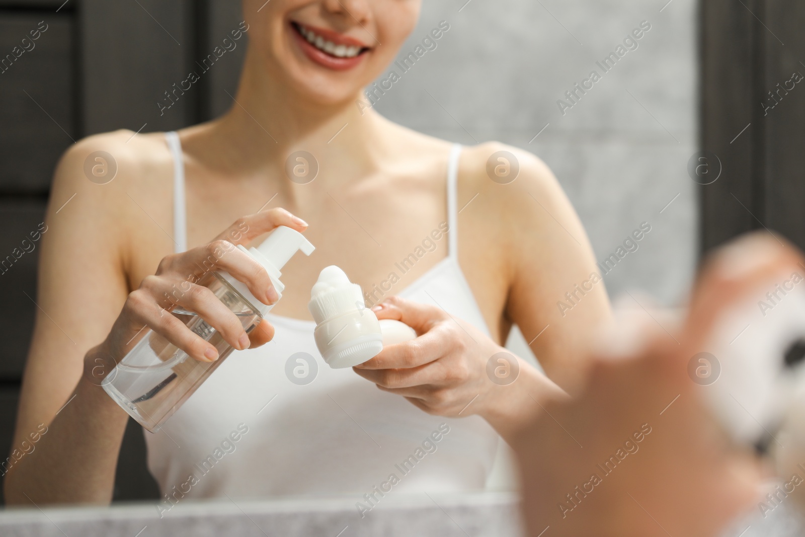 Photo of Washing face. Woman applying cleansing foam onto brush near mirror in bathroom, closeup