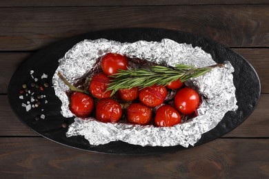 Aluminum foil with delicious baked tomatoes and rosemary on wooden table, top view