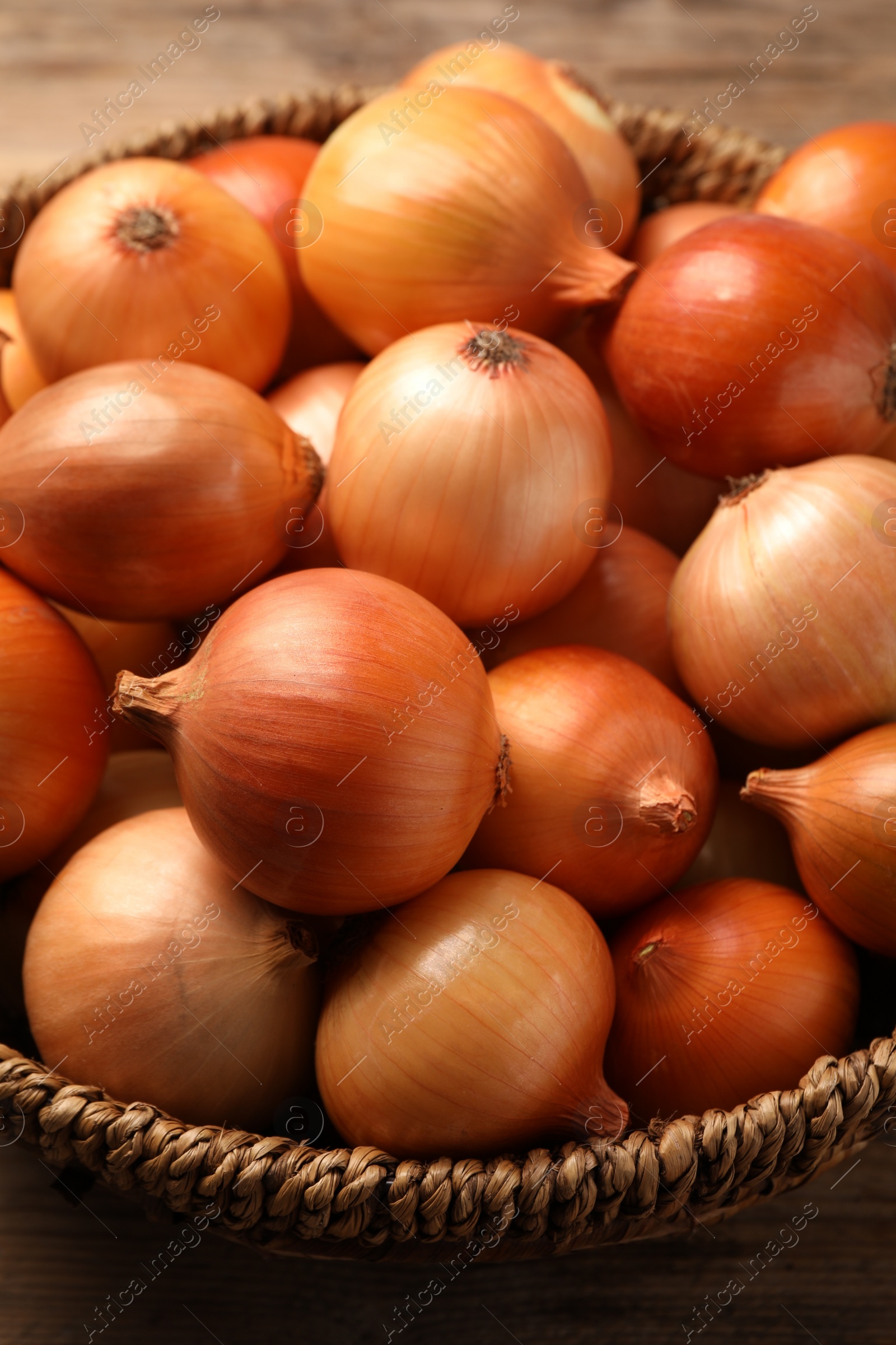 Photo of Wicker basket with many ripe onions on table, closeup