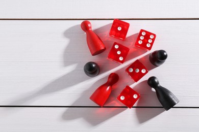 Photo of Red game dices and pieces on white wooden table, flat lay. Space for text