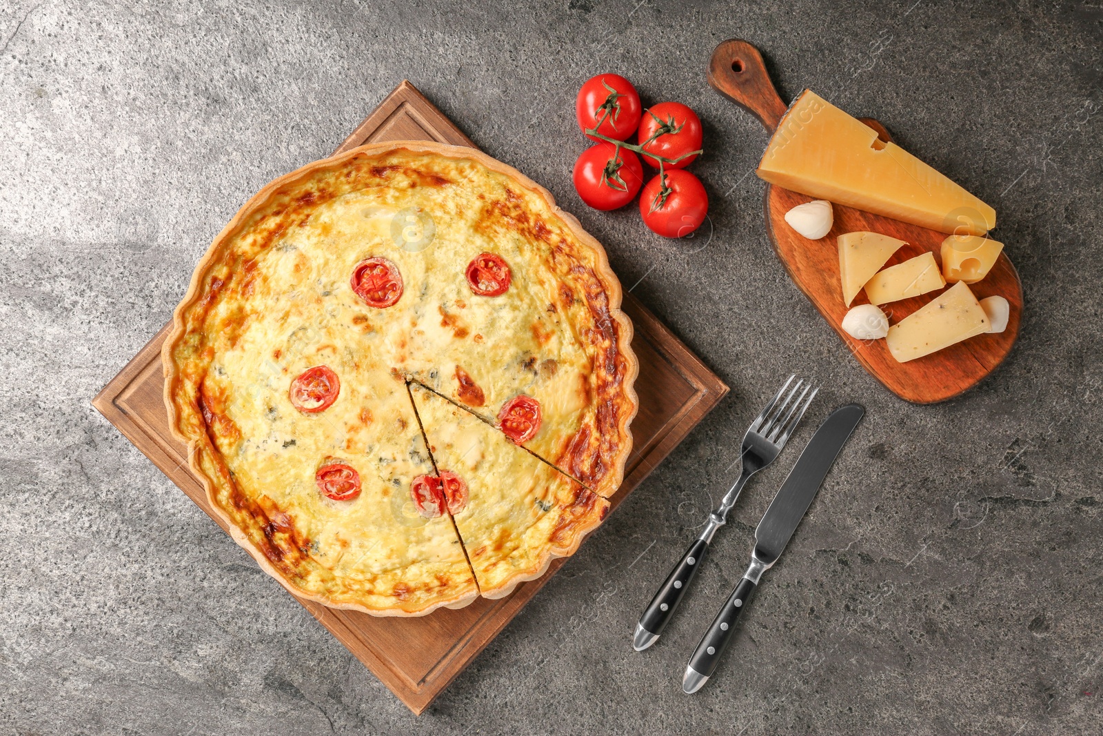 Photo of Delicious homemade cheese quiche, cutlery and ingredients on gray table, flat lay