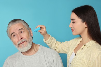 Young woman dripping medication into man's ear on light blue background