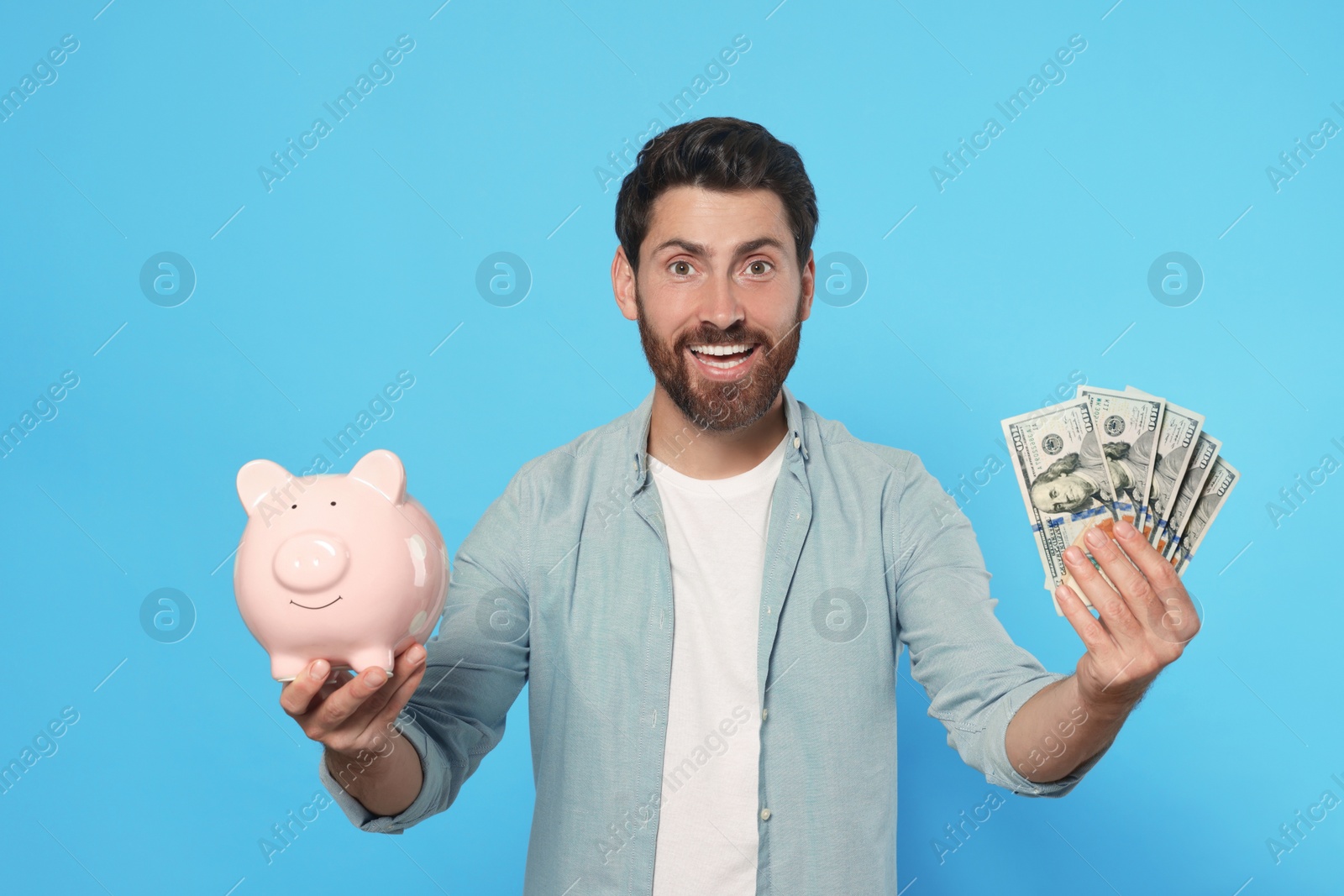 Photo of Happy man with money and ceramic piggy bank on light blue background