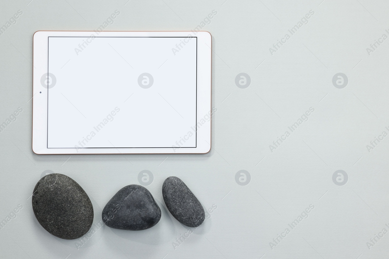 Photo of Modern tablet and pebbles on light grey background, flat lay. Space for text