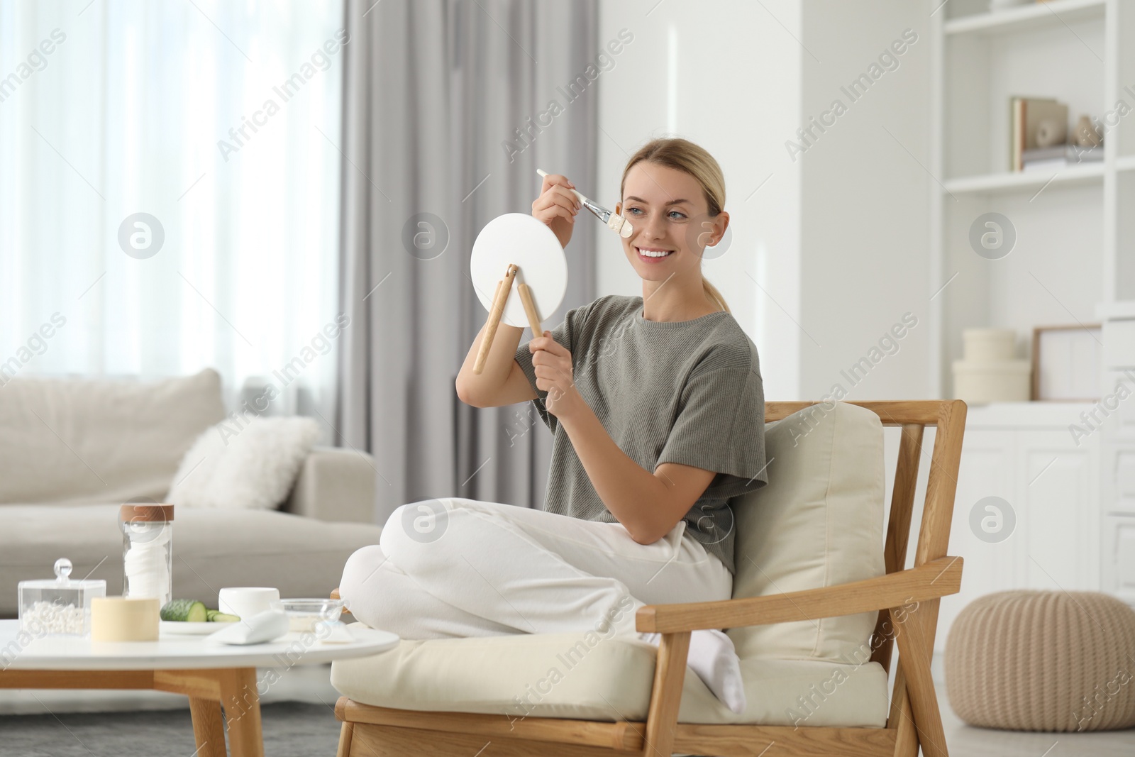 Photo of Young woman applying face mask in front of mirror at home. Spa treatments