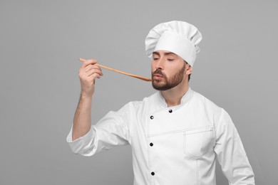 Photo of Mature chef with spoon tasting dish on grey background, space for text