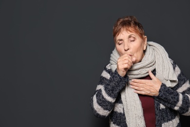 Photo of Elderly woman coughing against dark background. Space for text