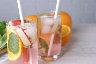 Photo of Tasty rhubarb cocktail with orange on white wooden table, closeup. Space for text