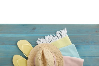 Light blue wooden surface with beach towel, hat and flip flops on white background, top view