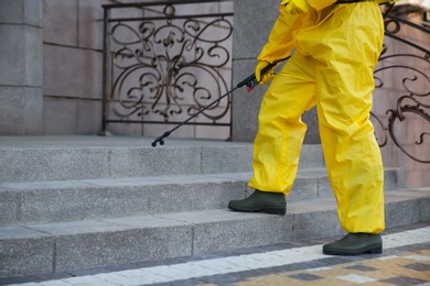 Photo of Person in hazmat suit disinfecting stairs with sprayer outdoors, closeup. Surface treatment during coronavirus pandemic