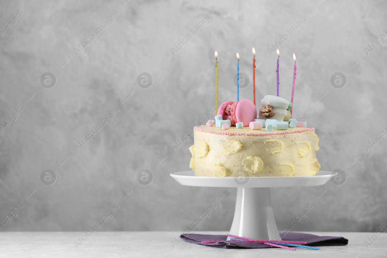 Photo of Delicious cake decorated with macarons, marshmallows and burning candles on white table against grey background, space for text